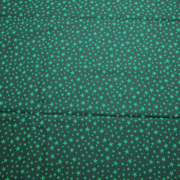A photo of Christmas everyday by Ann Wanke. The fabric has a dark green background with lighter colored green stars. The stars are a variety of sizes. The fabric was made by Henry Glass and company.