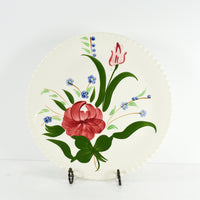 Shown is a Hand painted Southern Pottery dinner plate. This is the Bluebell Bouquet pattern on a slightly off white plate. The plate has a candlewick pattern on the rim. It is shown standing on a black metal plate stand. Photographed on a white background.