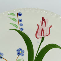 Another close up of the hand painted details on the Southern Pottery dinner plate. It shows some bluebells and a tulip type flower that has a lighter pink color with a darker pink or red highlights.