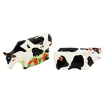 Seen are a pair of vintage Mann cow salt and pepper shakers. One cow is standing and the other cow is laying down. Both have horns.