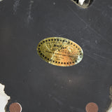 A close up of the gold foil label on the bottom of the base. It states Big Sky Carvers Presents Bear Foots "Mooses". Moose to Amuse and Collect. Made in China, 2000. There are small stars all the way around the oval label.