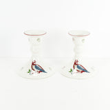 Shown are a pair of vintage Johnson Brothers 12 days of Christmas candlesticks. These feature a pair of blue and red partridges on each candlestick along with some green and red pears. The candlestick are white and shown on a white background.