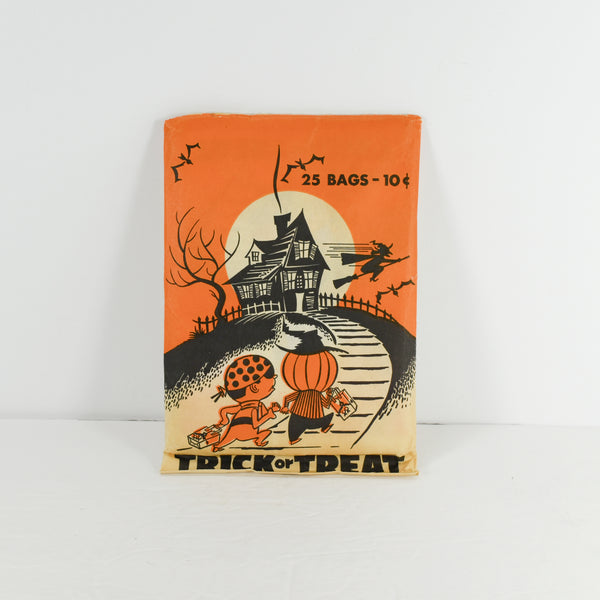 Shown is a vintage Halloween paper package that contains 25 trick or treat bags. Original price was 10 cents! It show two children in Halloween costumes running up to a spooky house. On the bottom in black lettering it states Trick or Treat. To the right of the house is a witch on a broom. To the left of the house is a black tree. It was photographed on a white background.