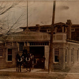 Shown is a partial view of the 1910 photograph postcard of what looks like a fire station, possibly from the Port Huron area of Michigan. The fire station is No. 4. There is a team of horses hitched to a wagon, that is in the double door entry way of the building. There is a man in a hat, sitting on the wagon holding the reins. There is a man in a cap with his hands clasped in front, standing to the wagon's left.