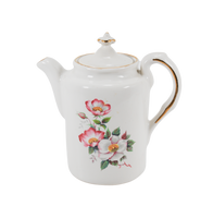 Featured is a vintage House of Webster teapot with the Wild Briar Rose pattern. The teapot was created prior to 1998. The teapot is white with gold trim on the edge of the handle and the top 'button' on the lid.