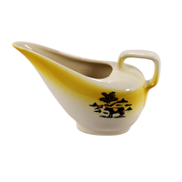 Shown is the vintage Grant Crest gravy boat from their Country Charm product line. This product line was produced in the 1950's. The gravy boat is a lovely creamy white color with a band of sunny yellow that encircles the upper edge. There is a cow in a pasture and a fence line and trees in the distance.