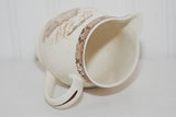 The creamer is laying on its side showing a partial view of the interior. There are some faint spots inside the interior from past use and age.