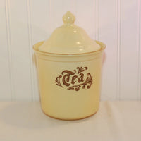 Featured ius a vintage Pfaltzgraff Tea Canister. It is the Village pattern and was made circa 1976-1980's. The piece is a creamy yellow with brown writing and design on the front. The canister has a lid.
