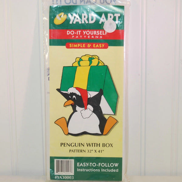 Shown in this photo is the front of the Yard Art. It is green, red, yellow and white in color. The words say, Do-it yourself patterns, Simple & Easy. There is a cartoon penguin sitting, holding a green and yellow Christmas package on his back. The penguin is wearing a red and white Santa hat. The pattern that can be made is a penguin with box. The pattern is 32 inches by 41 inches. 