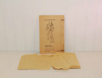 In this photo the paper instruction sheet is seen propped up on a white wall with the tissue paper sewing pattern laying in front of it. It is also on a white background.