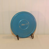 Shown is a round metal movie reel canister. It is blue in color and made by the Compco Corporation which was located in Chicago, Illinois. It is upright on a display stand and shown on a white background.