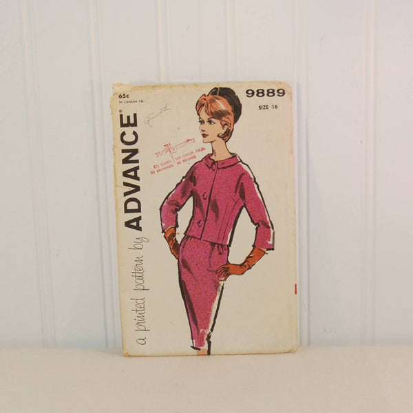 Shown is a c. 1960's skirt and jacket sewing pattern envelope. It was produced by Advance and is sewing pattern 9889. Shown is a hand drawn woman wearing a dark pink jacket and skirt. She is wearing gloves and a pill box black hat.