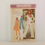 Featured is the front of the paper envelope for Simplicity 6104 circa 1973. It shows two illustrated women one in a skirt and blazer, the other woman has her back to us and is dressed in flared pants and a blazer. To the right of the two women there is a photo of a woman dressed in a white outfit consisting of flared pants and a blazer with buttons. She also has on a red and white scarf.