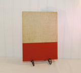 Shown is the back cover of the 1938 yearbook The Norwester. The top three quarter of the book is a cream color and the bottom quarter is an orange red color. It is propped up on a metal stand.