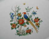 A close up of the center decor of the platter, there are flowers on a small tree, mushrooms at the base, the bird perched on a branch and a two butterflies flitting about.