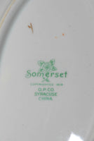 A close up of the backstamp. It is green in color and has a flower with the word Somerset just below the bloom. Under that it states: copyrighted 1919, O.P.CO., Syracuse, china.