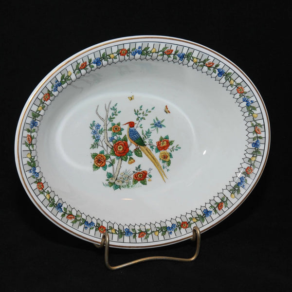 Shown is a beautiful example of Onondaga Pottery. It is the Somerset pattern and is an oval vegetable bowl. Circa 1919-?. There is a beautiful multicolored bird that could be a type of pheasant sitting on a branch of a small tree. There are also flowers on the tree. The border has rectangular design with an overlay of flowers. The bowl is white.