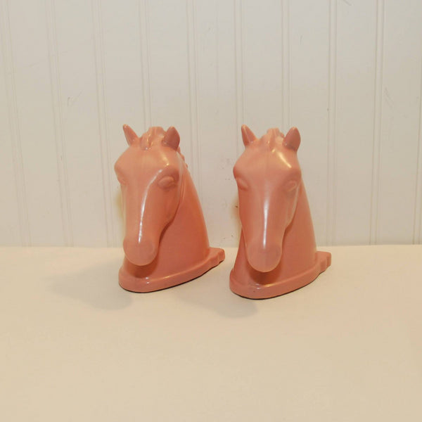 Shown in the photo are to matte pink horse head bookends created by Abingdon pottery. The horse heads are facing forward and the background is white.