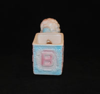 The back view of the Relpo lamb planter. There is the letter B in pink on the back and is surrounded by a baby blue color. The opening of the planter can be seen and it what is the cart that the lamb is pulling.