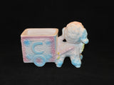 A back view of the lamb planter. The letter C can be seen on this side and it is baby blue in color. The cart has two wheels (not actual wheels however), one on each side.