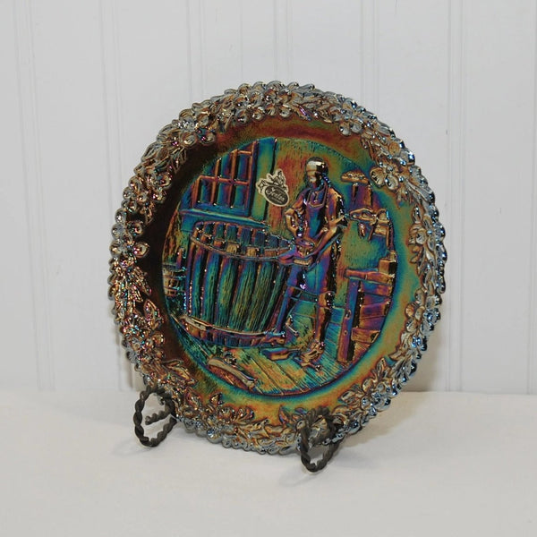 The front of the vintage Fenton commemorative plate of John Alden, number 5 in the series. There is a Fenton label on the front. The plate is made of carnival glass and is on a black plate stand. There is a floral decor all around the rim of the plate.