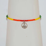 Shown is a Pride seed bracelet that has red seeds beads in the center, with a metal peace sign charm in the middle of that. Then there is orange, yellow, green seed beads on either side. The bracelet is shown on a vintage white hand form (not included). The Pride bracelet was handcrafted by Too Hip Chicks.
